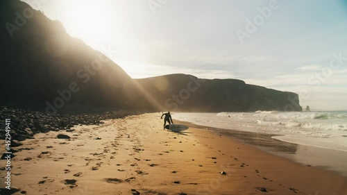 Surfer prepares to go into cold ocean water, stretch and attach leash to ankle. Safety and preparation for extreme sport. Big wave surfing in portugal. Cinematic and inspiring surfing lifestyle image