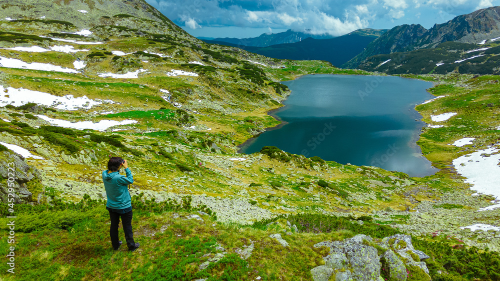 Landscape photography in an mountain range with a female photographer capturing the beautiful landscape with a glacial lake and mountains. Photographer capturing the beautiful scenery 