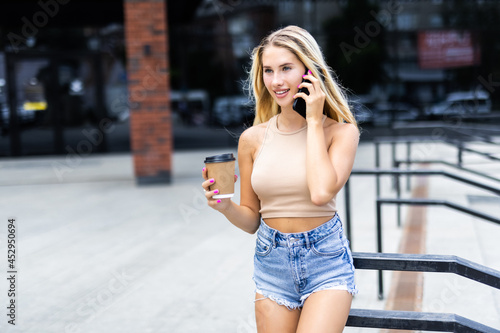 Beautiful young woman drinking coffee and talking to the phone in the street