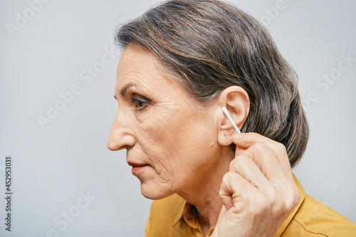 Mature woman cleans her ear from earwax with a cotton swab. Side view photo