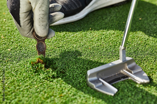 Golfer properly repair a divot mark on putting green using divot tool. Ball mark repair tool or divot tool on golf turf, close-up photo