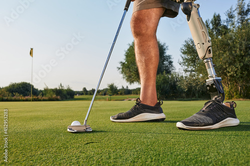 Professional golfer with prosthetic leg hitting with putter on golf ball during golfing. Concept of willpower of people with disabilities in sport photo