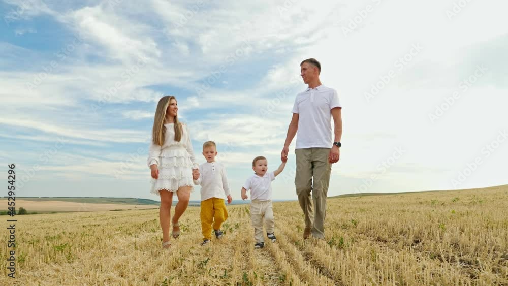 Family father mother and small children sons walk joining hands among field on mown wheat on sunny day under blue sky Family father mother and small children sons walk joining hands among field on mown wheat on sunny day under blue sky