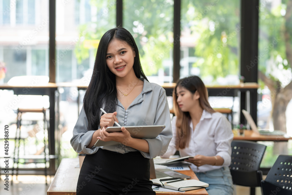 Fototapeta premium Front view of young Asian businesswoman holding a stylus tablet working. Looking at the camera.