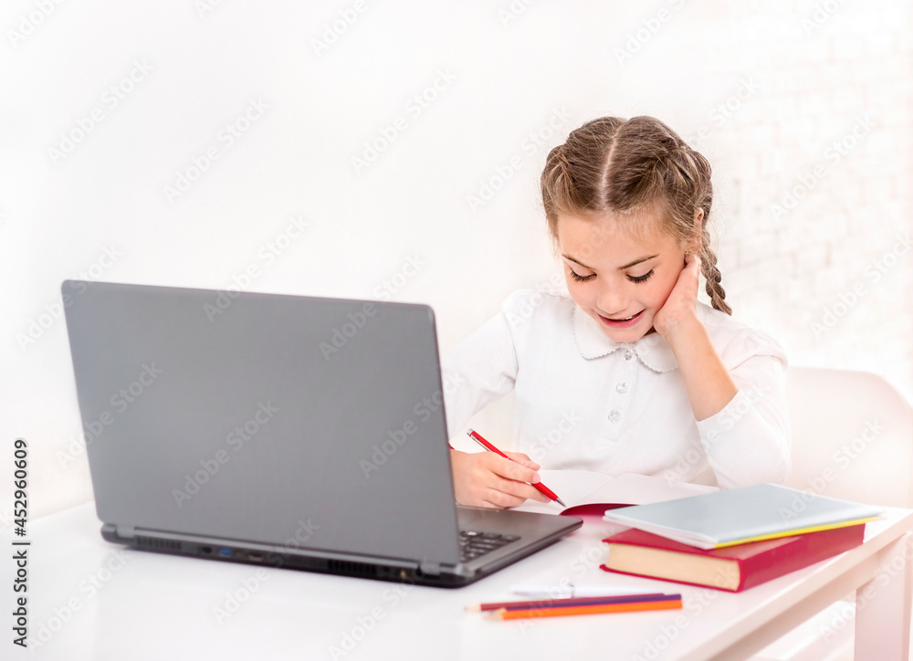 Schoolgirl learns at the table in front of the laptop Schoolgirl learns at the table in front of the laptop
