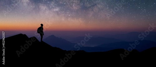 Panorama silhouette of young traveler with backpack standing and watched the star and milky way alone on top of the mountain. He enjoyed traveling and was successful when he reached the summit.