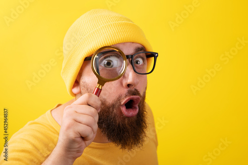 shocked man with magnifier over yellow background photo