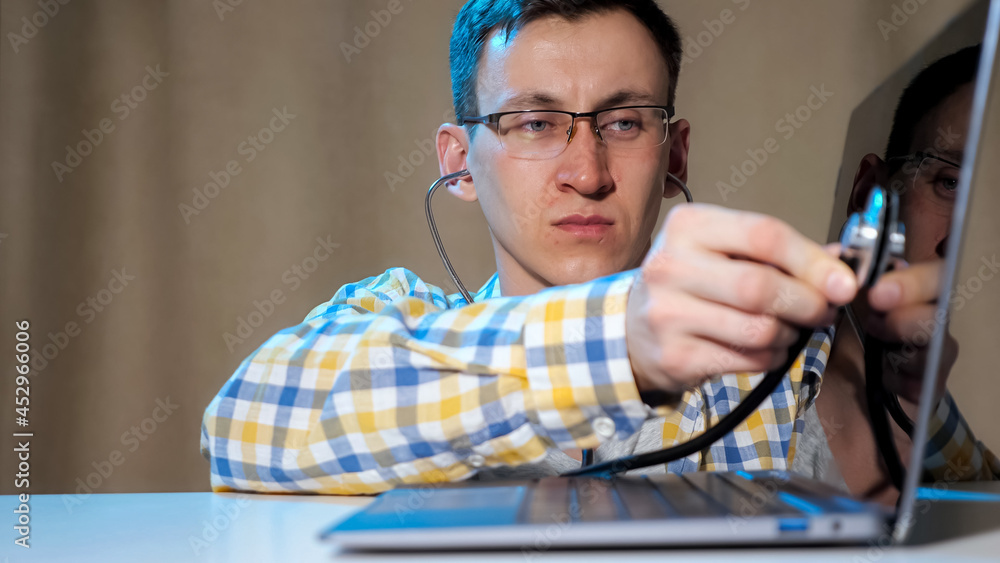 Young man diagnoses laptop using a phonendoscope.