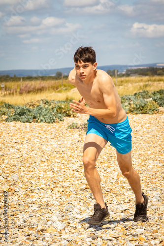Shirtless teenage boy running on a beach © Ben Gingell