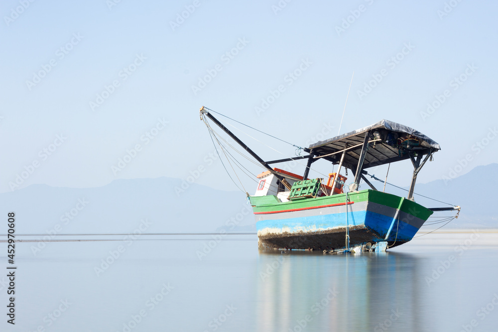Obraz premium Long exposure of a wooden fishing boat stranded on the beach in a shine day