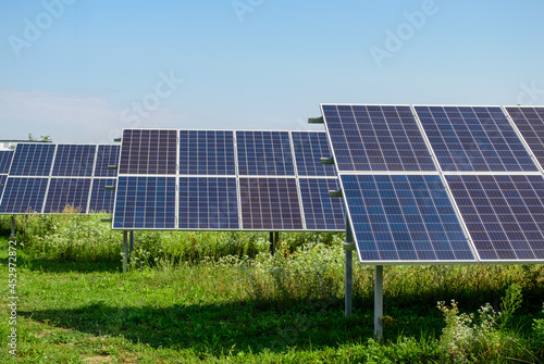 Solar panels front view in green field under clear blue sky on a sunny day