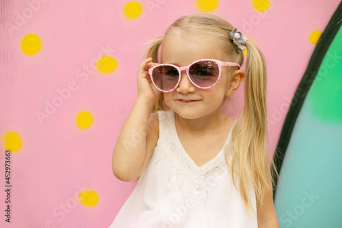 A little girl in pink glasses poses on pink