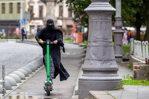 Muslim woman in a burqa rides a scooter in the city.