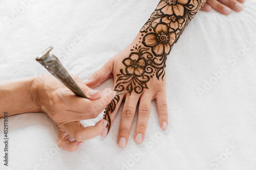 Top view art henna tattoo on woman hands. master artist drawing Arabic mehndi for bride before wedding. Close-up, overhead view. Floral design. Cone photo