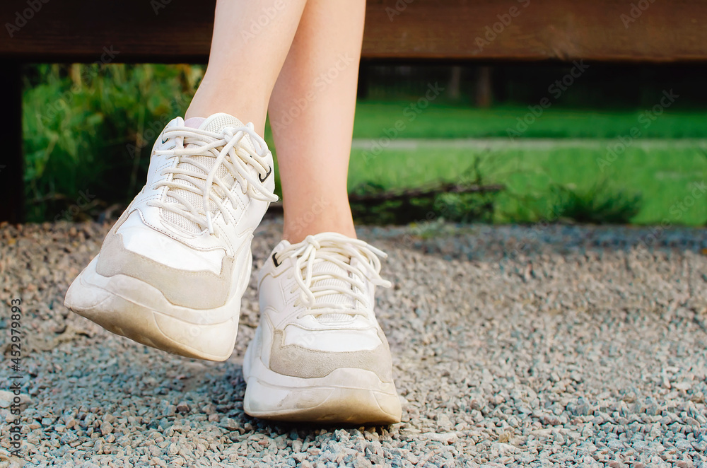 Legs of a young girl, shod in white sports sneakers, close-up.