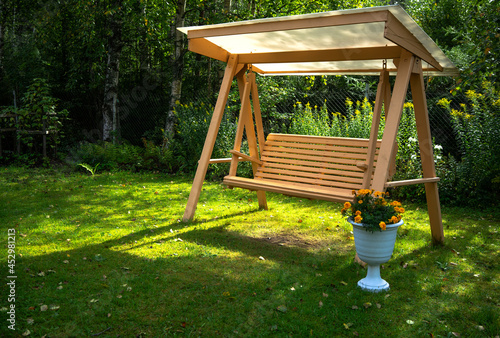 Принти на полотні Wooden garden swing with a plastic roof in summer on the green grass, next to a pot of yellow flowers