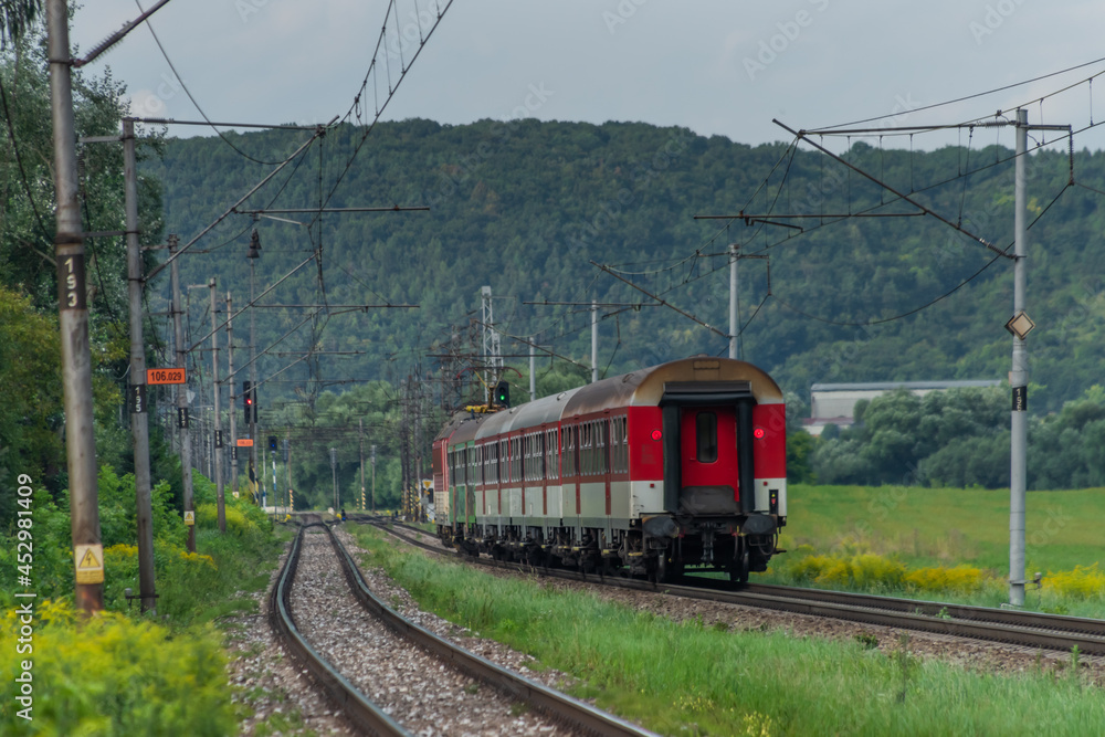 Fototapeta premium Passenger train with red electric locomotive and passenger coaches in summer