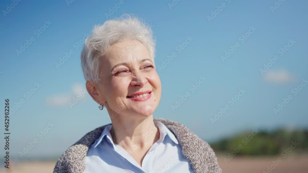 Head and shoulders portrait of senior woman with short gray short hair looking away and laughing. Happy mature female day dreaming against blue sky. Aging and happy retirement concepts Head and shoulders portrait of senior woman with short gray short hair looking away and laughing. Happy mature female day dreaming against blue sky. Aging and happy retirement concepts