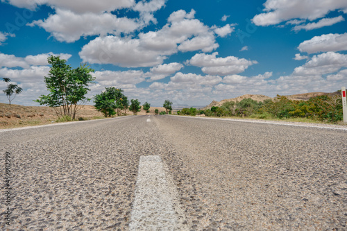 Gravel road and road sign by low angle photo in country side with cloudscape background with trees near the road in Konya Turkey