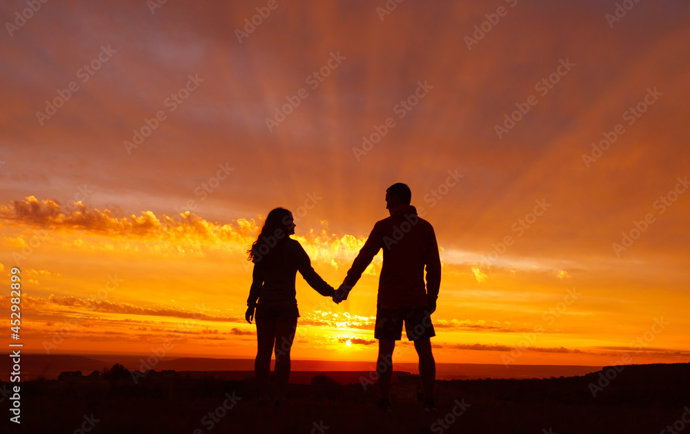 Loving couple stands against the backdrop of a beautiful fiery sunset. The sun's rays shine through the clouds. Romantic atmosphere.