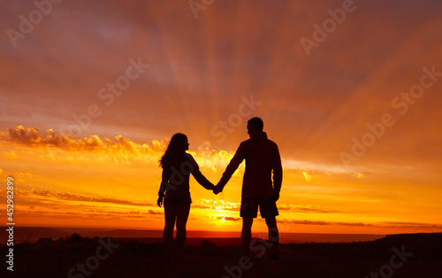 Loving couple stands against the backdrop of a beautiful fiery sunset. The sun s rays shine through the clouds. Romantic atmosphere.