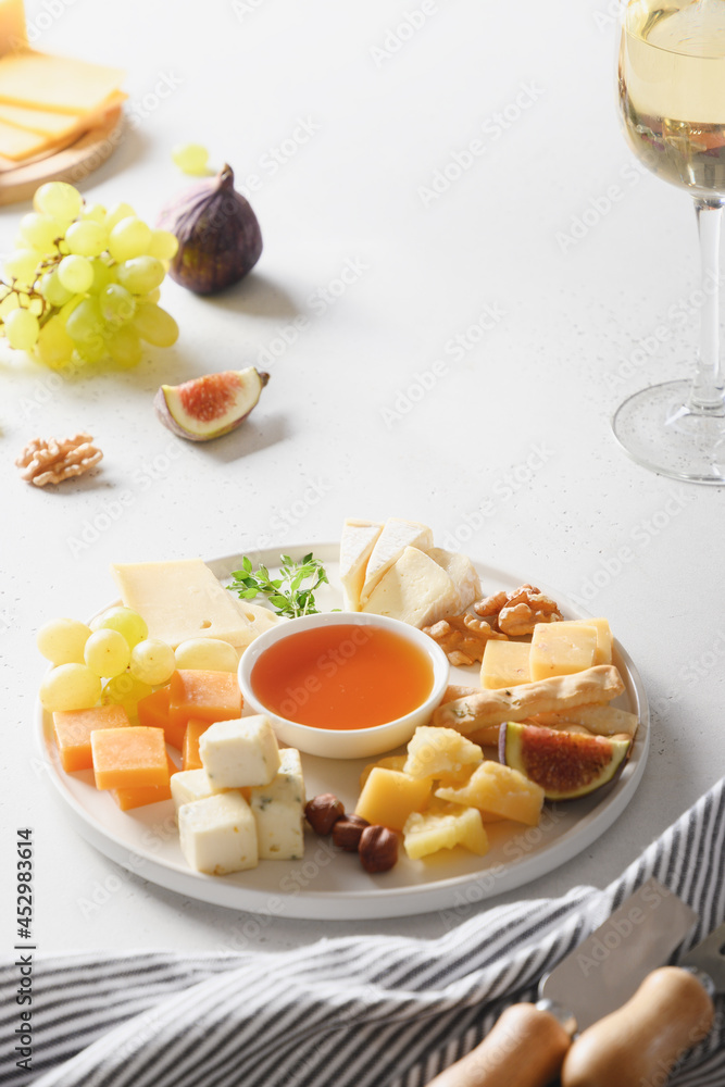 Cheese platter with grapes, nuts, figs on a white background. Vertical format. Festive gourmet snack. Cheese platter with grapes, nuts, figs on a white background. Vertical format. Festive gourmet snack.