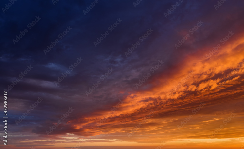 Vibrant sunset sky with dark clouds illuminated by orange sunlight