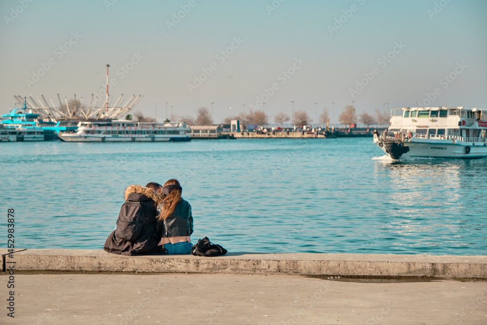 Turkey istanbul 04.03.2021. Two young couples and lovers hugging each other and sitting against bosporus in Kadikoy istanbul during sunny day with passenger ferry and turquoise water background.
