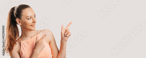 Portrait of a smiling girl pointing finger to the side at on a white isolated background. Positive woman points to an idea, a place for advertising