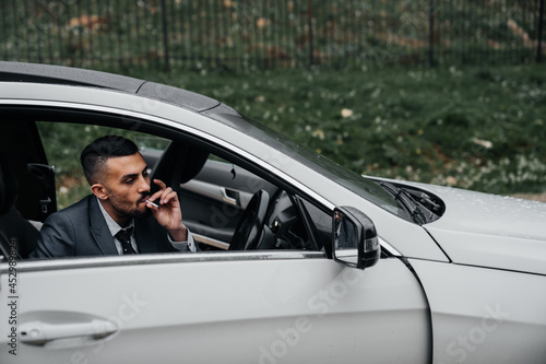 a man sits behind the wheel of a car with the door open and smokes a cigarette. © andrey