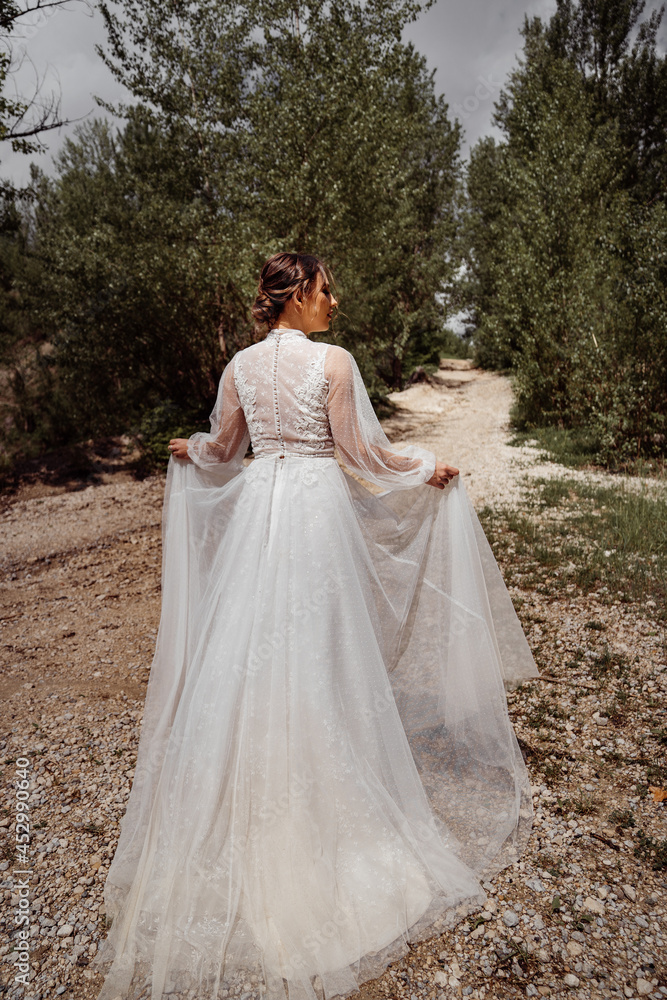 view from back. woman in wedding dress walks along mountain path between trees. view from back. woman in wedding dress walks along mountain path between trees.