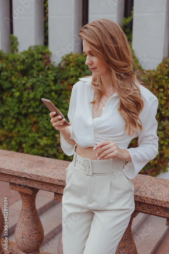 Schilderij op canvas Young woman in white clothing with mobile phone outdoors, woman chatting on her