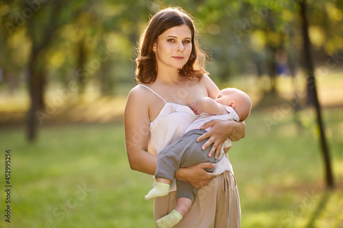 Breastfeeding in public park by young woman with baby. photo