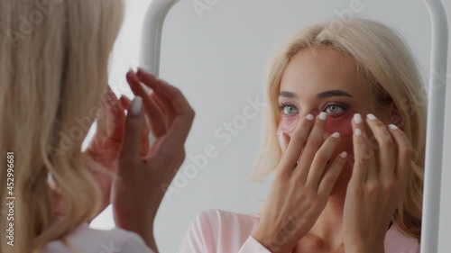 Beautiful Blonde Woman Applying Under-Eye Patches While Looking To Mirror At Home photo