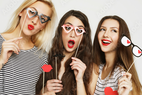 Three young women holding paper party sticks