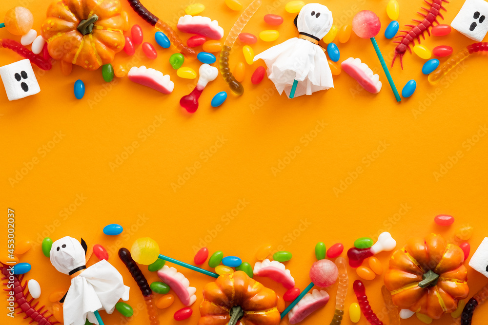 Obraz premium Happy Halloween holiday banner design. Frame border made of halloween decorations and candies on orange background. Flat lay, top view, copy space.