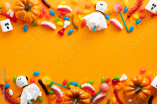 Happy Halloween holiday banner design. Frame border made of halloween decorations and candies on orange background. Flat lay, top view, copy space.