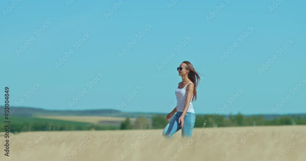 Beautiful young woman is walking across the field, she is smiling and happy. Woman with long hair and sunglasses walks in a golden field. Beautiful rural landscape. 4k, ProRes Beautiful young woman is walking across the field, she is smiling and happy. Woman with long hair and sunglasses walks in a golden field. Beautiful rural landscape. 4k, ProRes