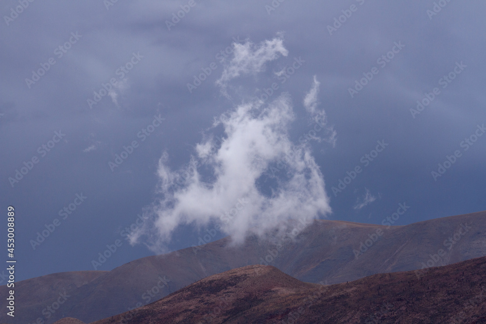 Fototapeta premium Poetic landscape. Single white cloud and mountain peak with a stormy sky background. 