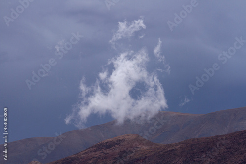 Poetic landscape. Single white cloud and mountain peak with a stormy sky background. 
