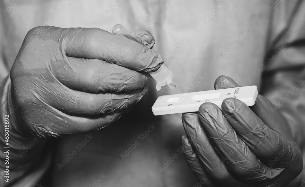 Black and White shot of healthcare worker squeezing drops of fluid after doing nasal swab for testing covid-19 by antigen test kit. Rapid antigen testing is a screening tool to help detect COVID-19.