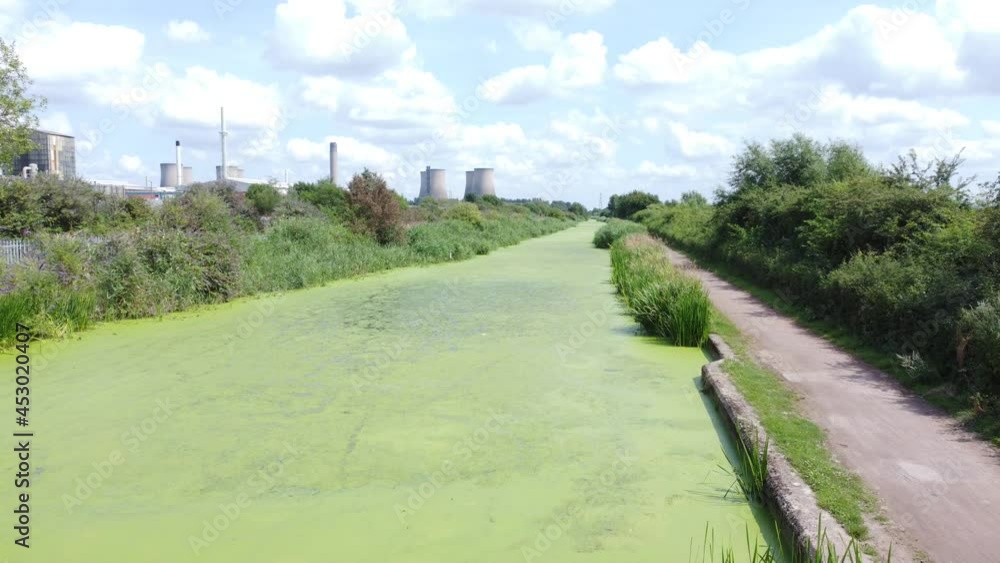 Green algae covered canal waterway leading to power station industry aerial drone view low forward shot