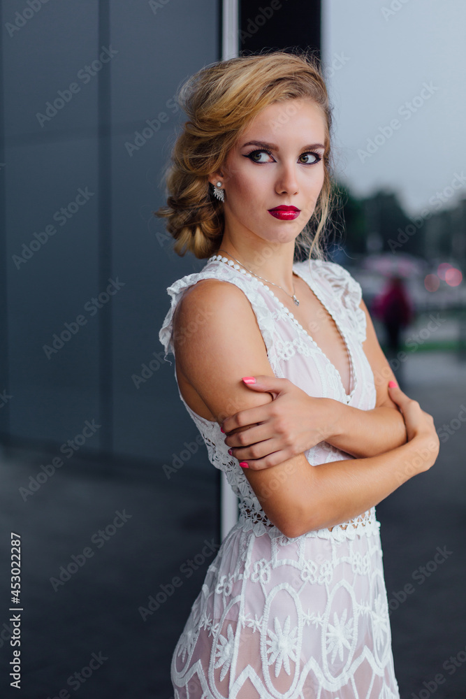 Fototapeta premium Beautiful blond bride in white wedding dress standing near mirror window outdoors.