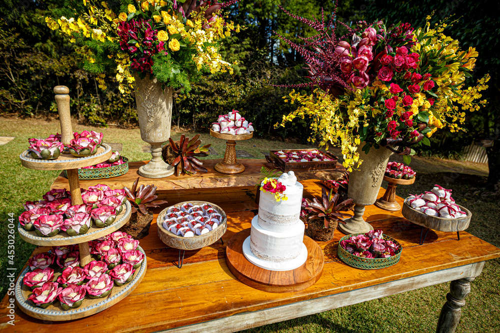 Mesa de bolo de casamento com pratos de doces e vasos de flores colorida em mesa rústica no jardim
