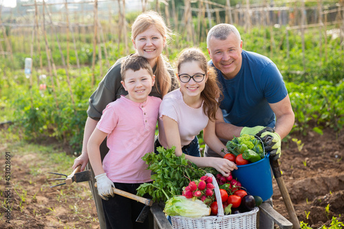 Parents with children posing with a basket of ripe vegetables in the garden