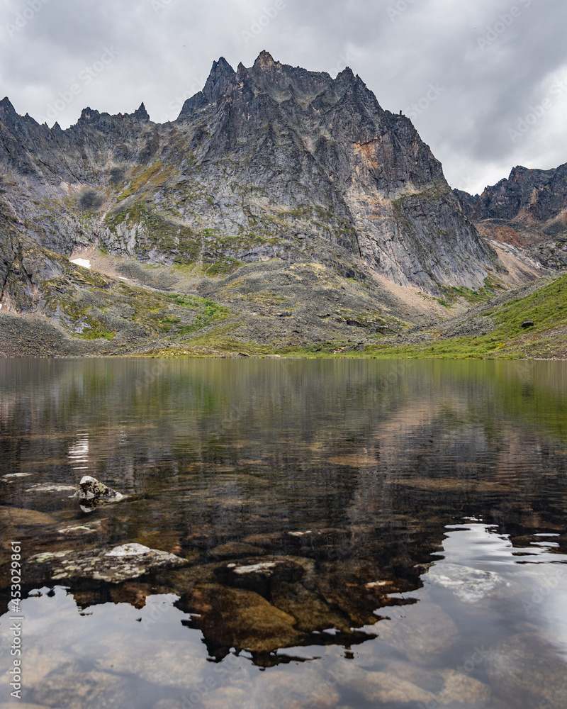 Stunning lake in Yukon, Canada during a cloudy summer day with reflection of mountain peaks in the calm Grizzly Lake below. 
