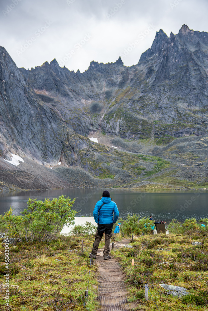 Man in blue jacket, black and brown pants admiring the view from Grizzly Lake backcountry campground in Tombstone Territorial Park, Yukon. 