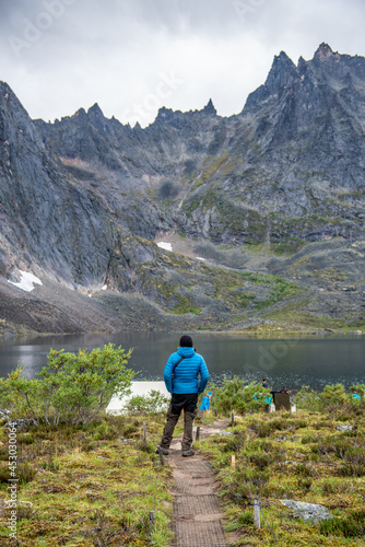 Man in blue jacket, black and brown pants admiring the view from Grizzly Lake backcountry campground in Tombstone Territorial Park, Yukon. 