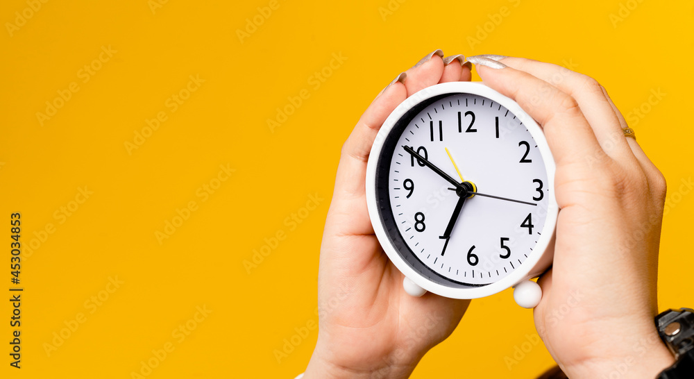 hand and alarm clock close-up white clock on a yellow background concept of waking up on time hand and alarm clock close-up white clock on a yellow background concept of waking up on time