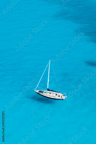 View from above, stunning aerial view of a sailboat floating on a turquoise, crystal clear water during a sunny day. Costa Smeralda, Sardinia, Italy.